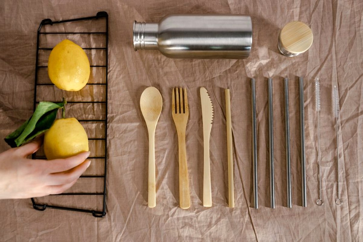 Reusable bottle, metal straws, wooden cutlery, and lemons arranged for a low-waste picnic.